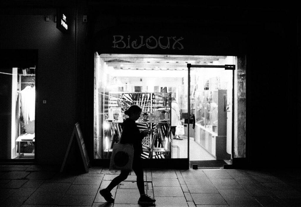 A person walking past an illuminated jewelry shop window at night, attention passing a store without having searched for it