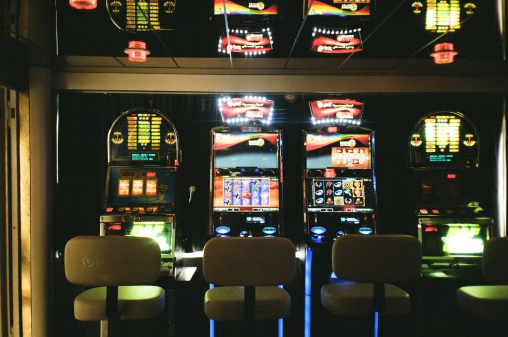 Lit slot machines blinking in a dark arcade with every stool empty, machines celebrating with nobody there